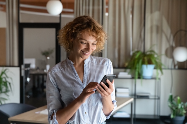 Smiling woman checking messages on her phone in a modern office.